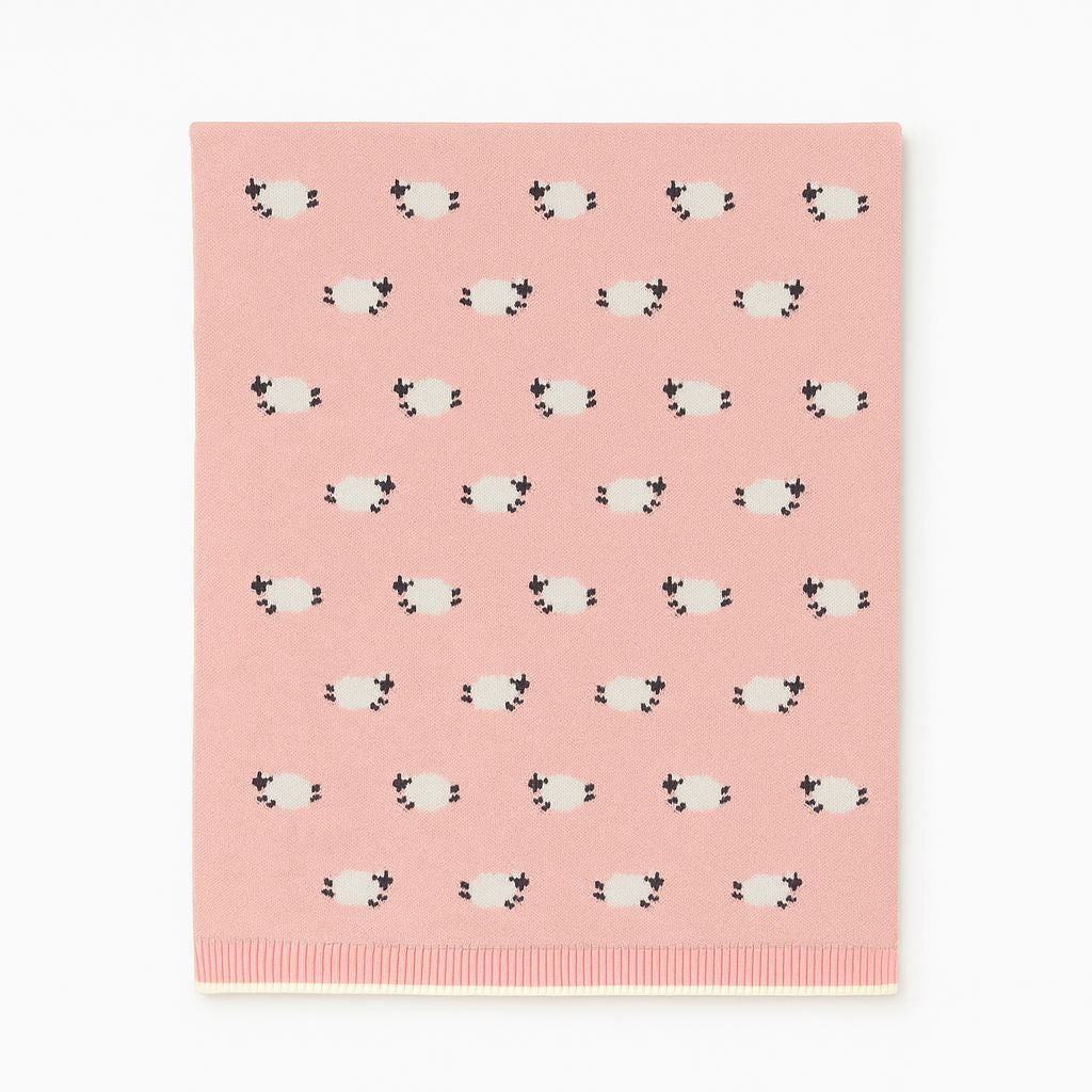 A pink rectangular fabric item, likely a blanket or towel, featuring a repeating pattern of small white sheep with black faces and ears. The bottom edge has a ribbed knit border.