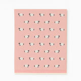 A pink rectangular fabric item, likely a blanket or towel, featuring a repeating pattern of small white sheep with black faces and ears. The bottom edge has a ribbed knit border.