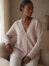 Woman wearing a light beige cashmere wool cardigan sitting on a couch in a cozy room.