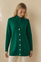 Woman wearing a luxury green cashmere wool cardigan with white buttons on a beige background