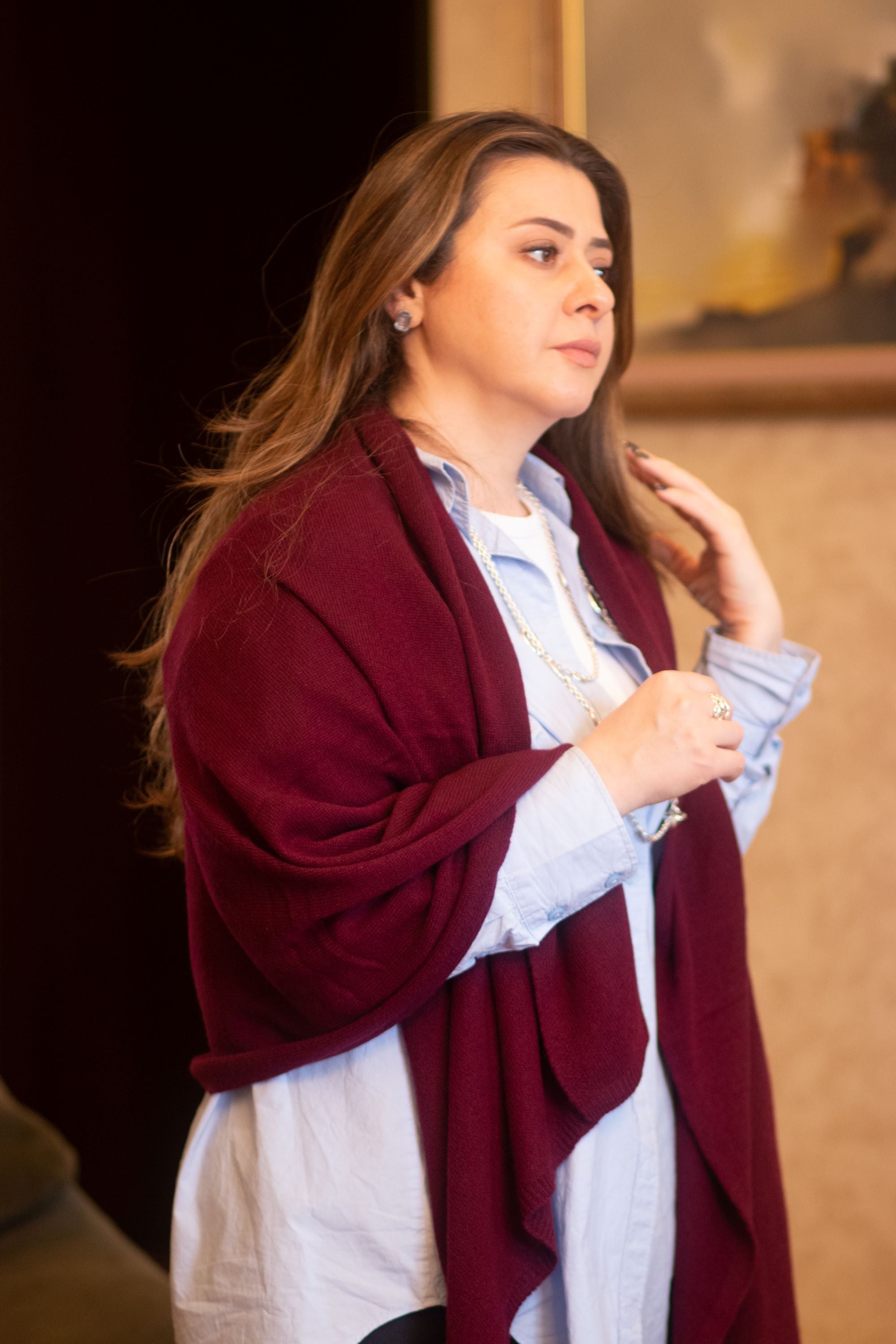 A person wearing a red cashmere scarf draped over the shoulders, with a light blue shirt and dark pants.