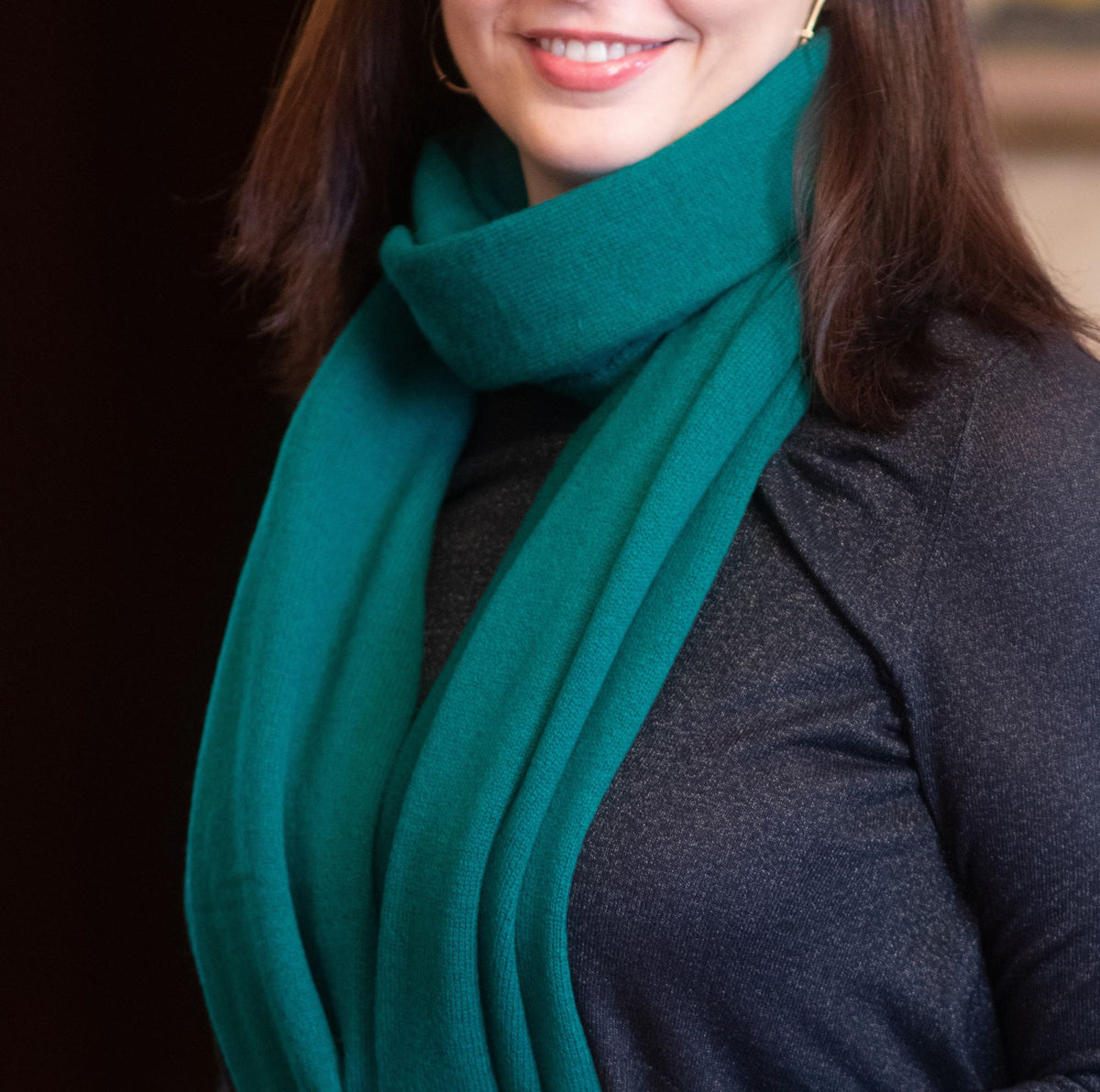 A close-up of a woman wearing a thick, solid teal green cashmere wool scarf wrapped around her neck over a dark gray top.