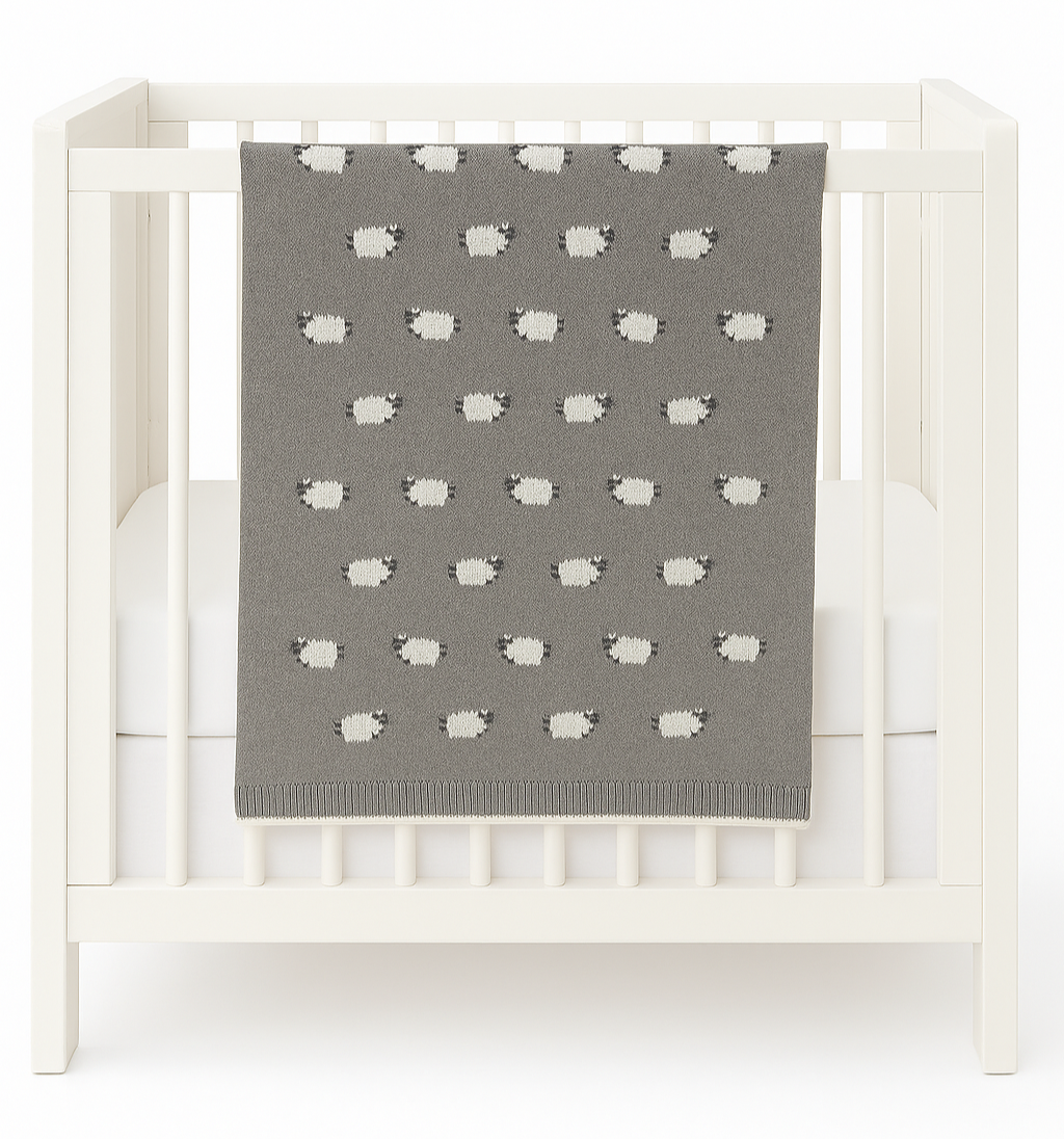 Gray baby blanket with white sheep pattern draped over a white crib.