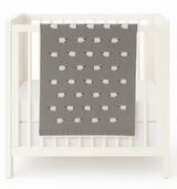Gray baby blanket with white sheep pattern draped over a white crib.