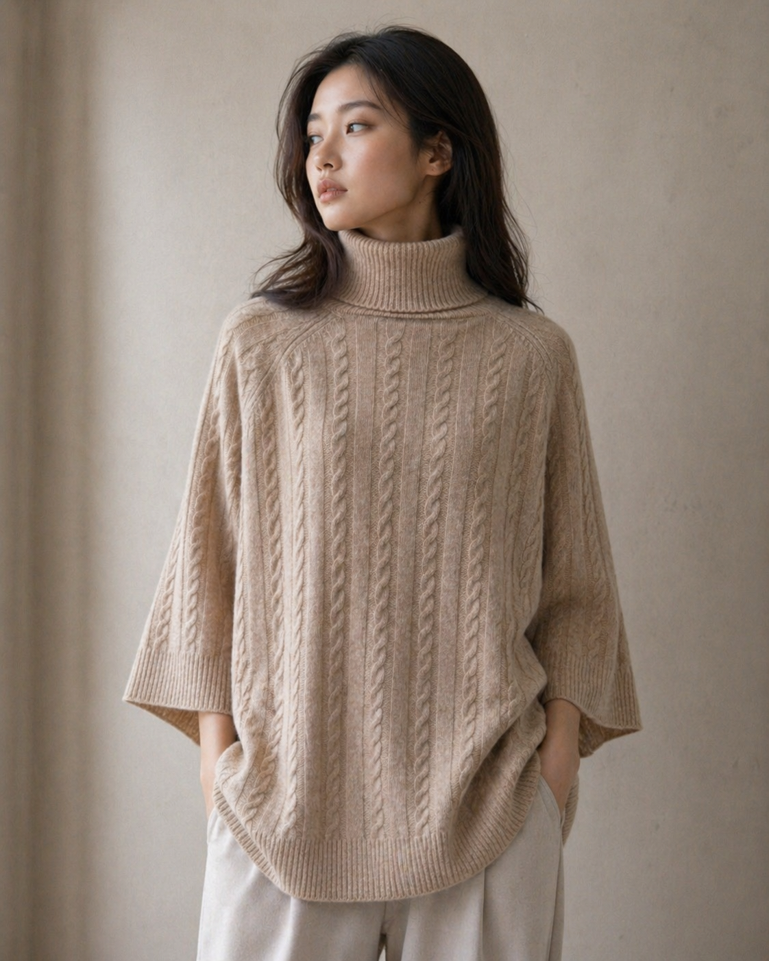 Woman wearing a beige cable turtleneck tunic knit sweater against a neutral background