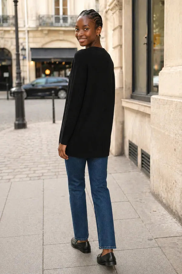 Person wearing a black sweater and blue jeans standing on a city street.