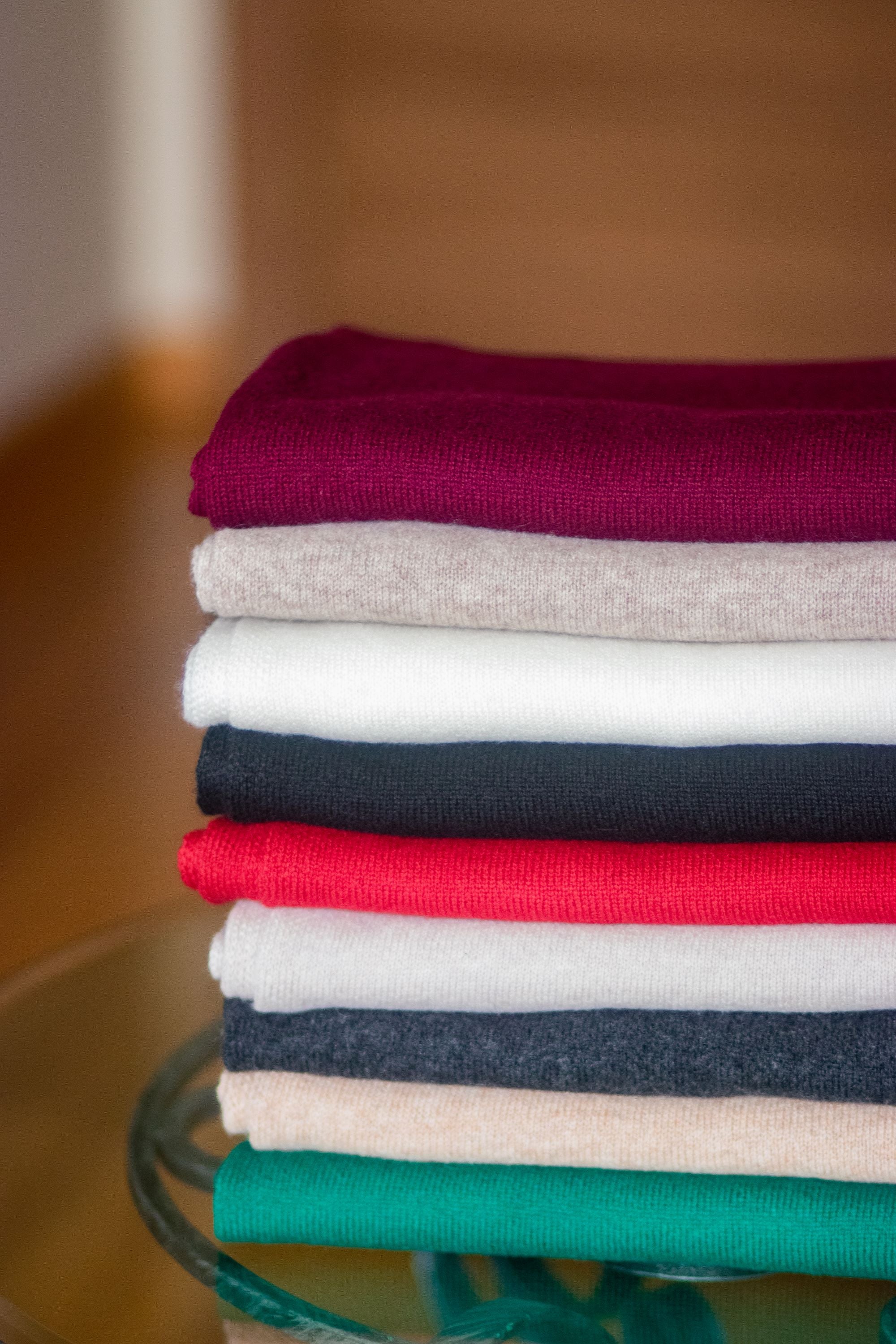 A stack of folded cashmere scarves in red, purple, white, and black colors, arranged on a glass surface.
