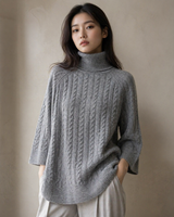 Woman wearing a gray Cable Turtleneckknit sweater against a neutral background