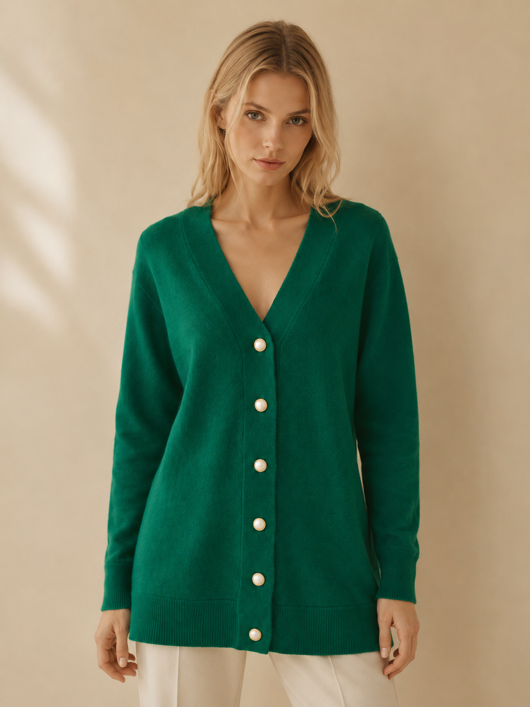 Woman wearing a green luxury cashmere wool cardigan with white buttons on a beige background